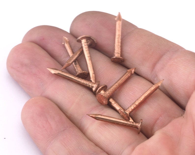 May include: A close-up of a hand holding a group of copper-colored nails. The nails are sharp and pointed, and they are arranged in a random pattern.