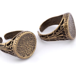 May include: Two antique gold-toned rings with ornate designs and round bezels. The rings are made of metal and have a vintage look.