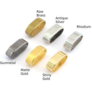 Op de afbeelding: Een close-up van tien ovale metalen ringen in verschillende afwerkingen: ruw messing, antiek zilver, rhodium, gunmetal, mat goud en glanzend goud.