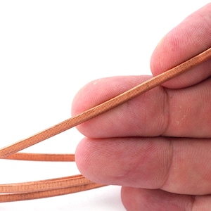 May include: A close-up of a copper wire with a ribbed texture. The wire is held in a hand, and the background is white.