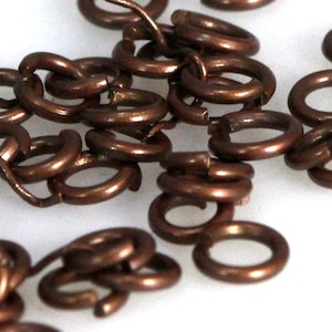 May include: A pile of small, copper-coloured jump rings. The rings are all the same size and are arranged in a random pattern.
