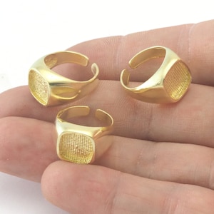 Puede incluir: Tres anillos ajustables de color dorado con parte superior cuadrada. Los anillos son de metal y tienen un acabado liso.