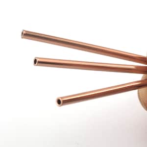 Op de afbeelding: Drie koperen drinkrietjes, elk met een afgerond uiteinde, worden in een waaier vorm gehouden.