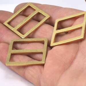 May include: Three gold-colored metal buckles with two horizontal bars. The buckles are on a hand.