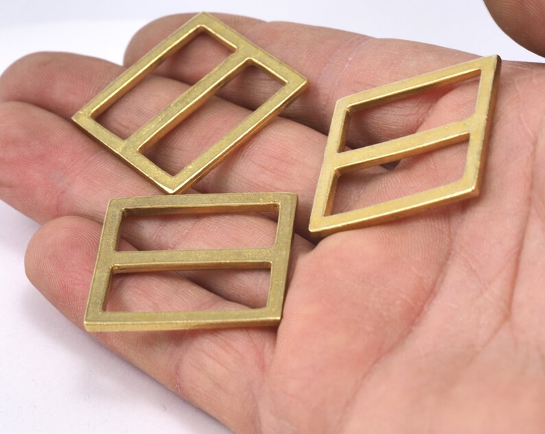May include: Three gold-colored metal buckles with two horizontal bars. The buckles are on a hand.
