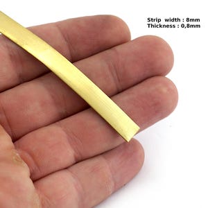 May include: A flat, rectangular brass strip, 8mm wide and 0.8mm thick, is held in a hand. The strip has a polished, golden appearance. The text on the image reads: Strip width: 8mm, Thickness: 0,8mm.