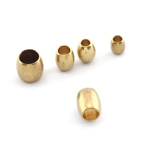 May include: Five gold-colored metal beads, some round and some oval, are arranged on a white surface.