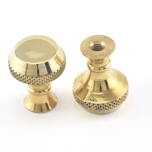 Puede incluir: Dos pomos de latón para armarios. Uno tiene la parte superior redondeada y una base con diseño de diamantes. El otro tiene la parte superior roscada y una base similar con diseño de diamantes. Ambos son de latón brillante sobre fondo blanco.
