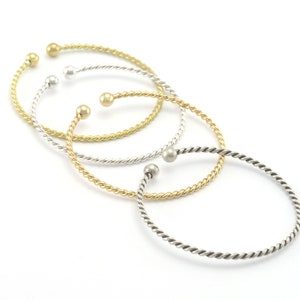 Può includere: Tre braccialetti in filo ritorto con chiusura a sfera. I braccialetti sono in oro, argento e argento scuro.