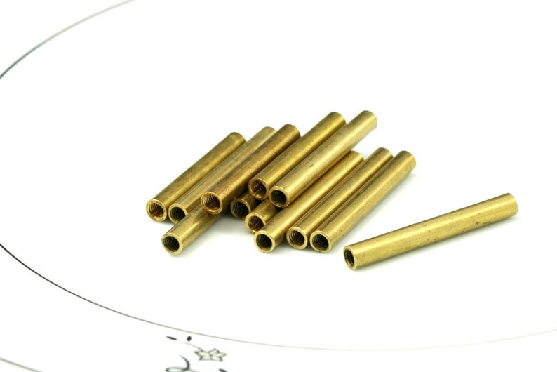 May include: A group of brass tubes, some stacked on top of each other, with a single tube lying horizontally in the foreground.