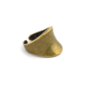 Peut inclure: Une bague de couleur bronze avec un design incurvé en forme de bouclier. La bague a une surface texturée et une large bande qui se rétrécit vers l'arrière. La bague est posée sur un fond blanc.