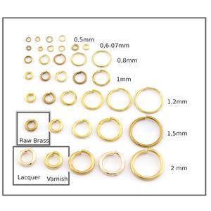 May include: Assortment of gold jump rings in various sizes, ranging from 0.5mm to 2mm. The jump rings are arranged in rows by size, with labels indicating the diameter of each ring. The jump rings are shown in three finishes: raw brass, lacquered, and varnished.