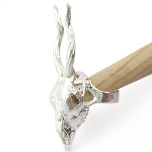 May include: A silver ring featuring a detailed deer skull design with antlers. The ring is shown on a wooden dowel.