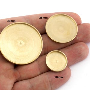 Può includere: Tre vassoietti rotondi color ottone di diverse dimensioni: 38 mm, 28 mm e 18 mm. I vassoietti hanno un design circolare poco profondo con un bordo leggermente rialzato. I vassoietti sono tenuti in mano, mostrando le loro dimensioni e forma.