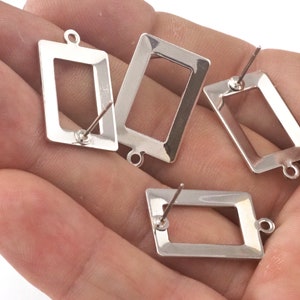 Puede incluir: Cuatro engastes para pendientes de color plateado con un marco rectangular y un poste para sujetar los pendientes. Los engastes están diseñados para sujetar un pequeño trozo de vidrio u otro material en el centro.