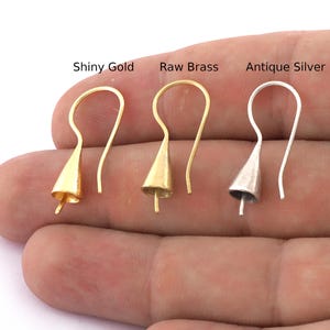 Può includere: Tre ganci per orecchini in diverse finiture: oro lucido, ottone grezzo e argento anticato. Ogni gancio ha una piccola estremità a forma di campana.