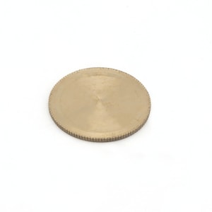 Op de afbeelding: Een rond, messingkleurig metalen object met een geribbelde rand. Het object is cirkelvormig en heeft een licht getextureerd oppervlak. De achtergrond is effen wit.