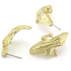May include: A pair of gold-tone alligator earrings. Each earring features a detailed alligator design with a post and butterfly backing.