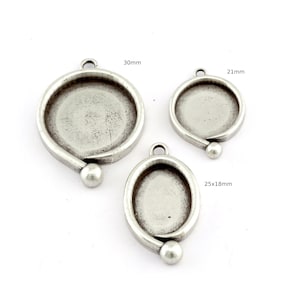 May include: Three silver-coloured pendant trays in different sizes. The largest is 30mm in diameter, the next is 21mm, and the smallest is 25x18mm. Each has a loop for hanging and a decorative ball at the base. For jewellery making.