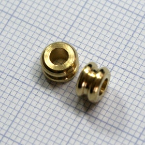 May include: Two gold-coloured metal beads with a smooth, rounded surface. The beads have a hole in the centre for stringing.