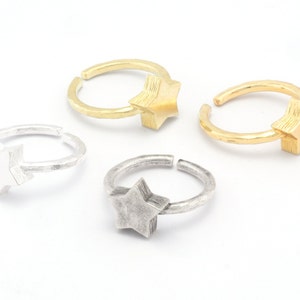 Puede incluir: Tres anillos ajustables con dijes en forma de estrella. Los anillos están hechos de metal plateado y dorado. Las estrellas son texturizadas y tienen un diseño en capas.