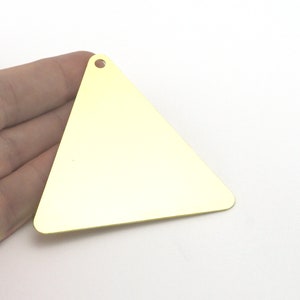 Peut inclure: Un pendentif triangulaire en métal doré plat avec une surface lisse et réfléchissante. La pièce présente un petit trou circulaire percé près du coin supérieur, conçu pour être fixé à une chaîne, un cordon ou un anneau pour la bijouterie.