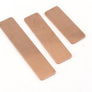 May include: Three rectangular pieces of copper metal, arranged in a descending size order. The metal has a warm, reddish-brown color.