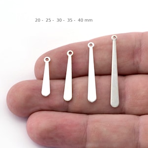 Peut inclure: Quatre breloques pendantes en forme de larme argentées de différentes tailles, mesurant 20 mm, 25 mm, 30 mm, 35 mm et 40 mm. Les breloques sont présentées sur une main, la plus petite à gauche et la plus grande à droite.