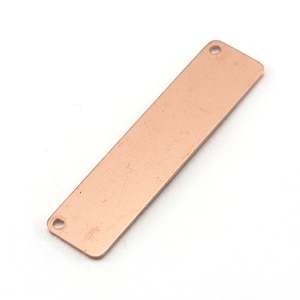 May include: A rectangular copper tag with two holes at the top and bottom. The tag is a blank surface for engraving or stamping.