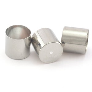 Könnte beinhalten: Drei silberne Metallkappen für eine Flasche oder ein Glas. Die Kappen sind zylindrisch und haben eine glatte, polierte Oberfläche.