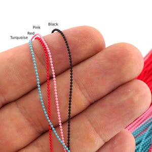 Può includere: Tre catenelle a sfere sottili nei colori turchese, rosso, rosa e nero. Le catene sono etichettate con il testo Turquoise, Red, Pink e Black. Ogni catena è composta da piccole perle sferiche uniformi collegate in un filo continuo.