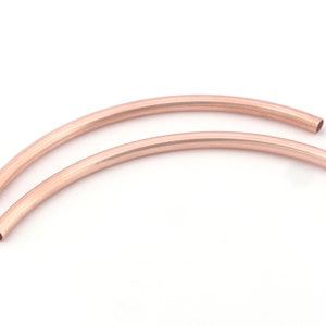 May include: Two rose gold colored metal hoops, each with a diameter of approximately 2 inches. The hoops are curved and have a smooth, polished finish.