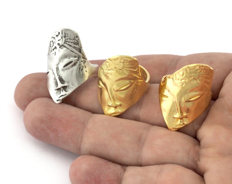 Peut inclure: Trois bagues en argent et en or avec un motif de visage. Les bagues sont sur une main.