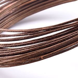 May include: A close-up of a spool of brown copper wire. The wire has a textured surface and is wound tightly around the spool.