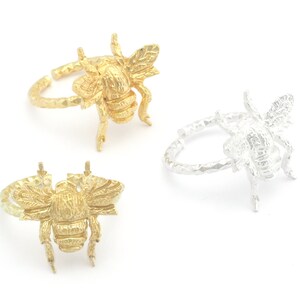 Op de afbeelding: Twee ringen in de vorm van een bij, een gouden en een zilveren. De ringen zijn getextureerd en hebben een gedetailleerd bijendesign.