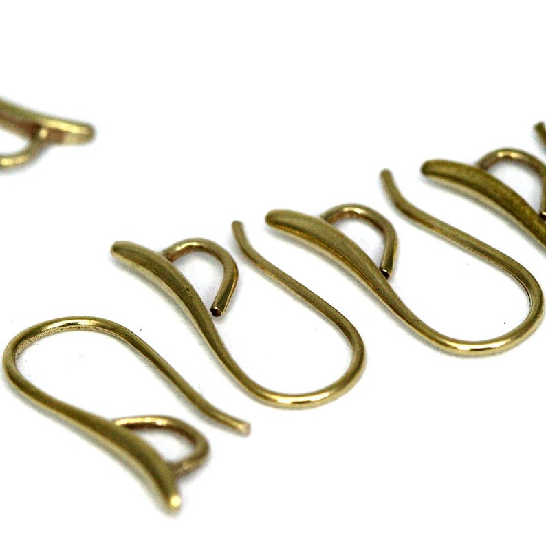 May include: Five gold-toned earring hooks, each with a curved, slightly flattened shape. The hooks are arranged in a row, with the tips of the hooks pointing in the same direction.