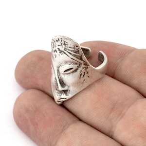 Peut inclure: Une bague en argent avec un design de visage d&eacute;taill&eacute;. La bague est ouverte d'un c&ocirc;t&eacute; et a une surface textur&eacute;e.