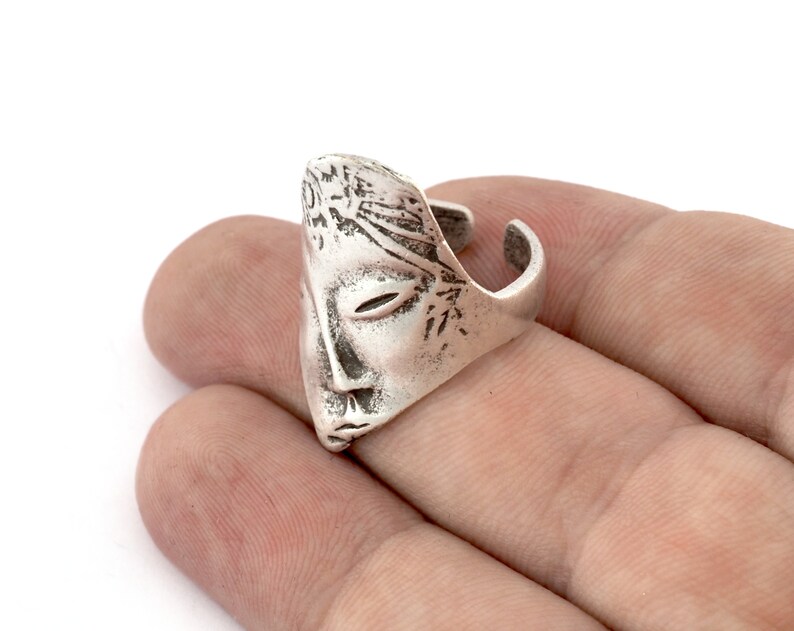 Peut inclure: Une bague en argent avec un design de visage d&eacute;taill&eacute;. La bague est ouverte d'un c&ocirc;t&eacute; et a une surface textur&eacute;e.