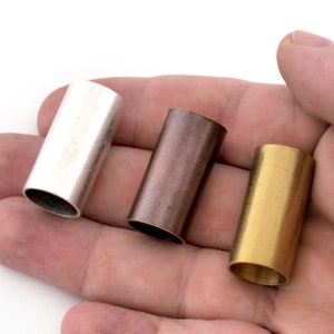 May include: Three metal tubes, one silver, one copper, and one gold, are held in a hand. The tubes are all the same size and shape.