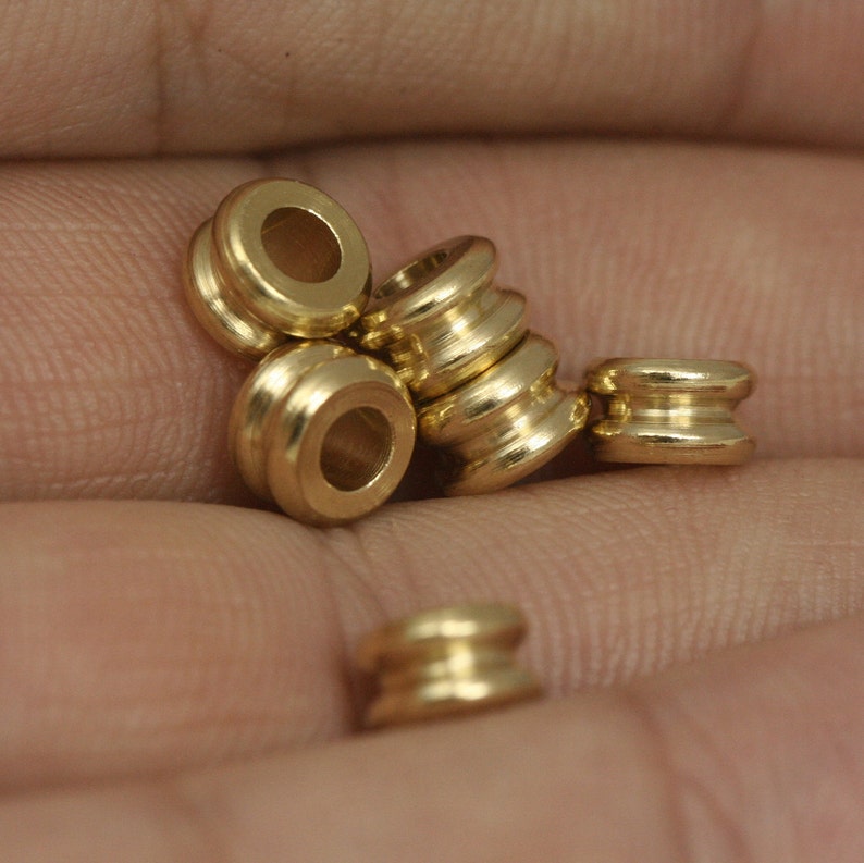 May include: A close-up of five gold-coloured metal beads. The beads are round and have a smooth, polished finish. They are arranged in a pile on a person's hand.
