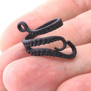 May include: A black octopus ring with textured details. The ring is made of metal and is designed to wrap around the finger.
