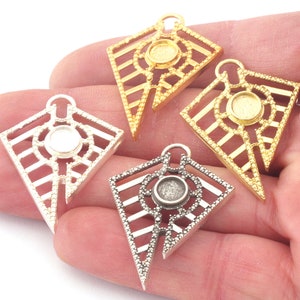 Może przedstawiać: Cztery metalowe zawieszki w kształcie geometrycznego diamentu z okrągłym oczkiem w środku. Zawieszki są w kolorze srebrnym, złotym i dwóch odcieniach złota.