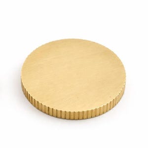 Op de afbeelding: Massief messing kastknop met een rond ontwerp. De bovenkant is glad, terwijl de zijkanten een geribbelde textuur hebben. De knop heeft een warme goudkleur. Geschikt voor laden en deuren.