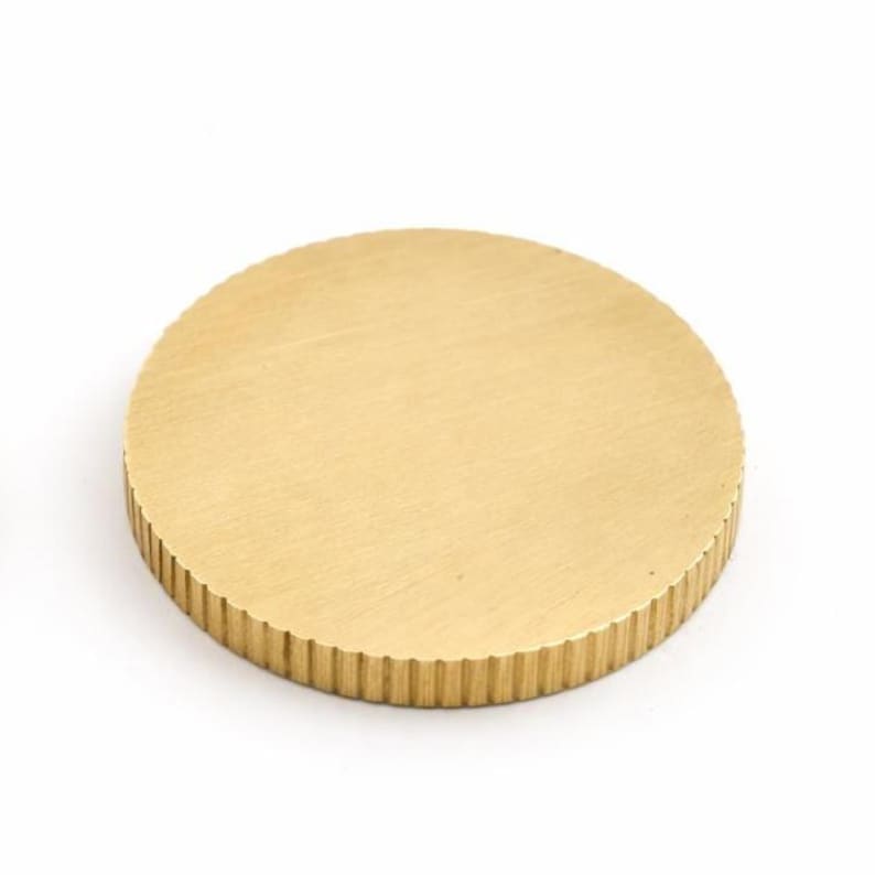 Op de afbeelding: Massief messing kastknop met een rond ontwerp. De bovenkant is glad, terwijl de zijkanten een geribbelde textuur hebben. De knop heeft een warme goudkleur. Geschikt voor laden en deuren.