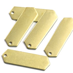 May include: Four gold-coloured metal tags with rounded edges and a hole at the top. The tags are arranged in a staggered pattern.