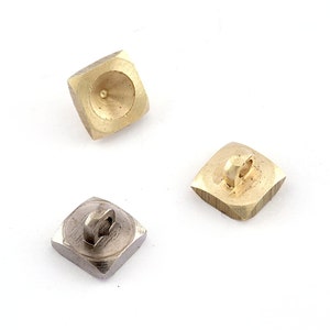 May include: Three square-shaped metal buttons. Two are gold-colored, and one is silver. The gold buttons have a concave back with a small hole. The silver button has a loop on the back for sewing.