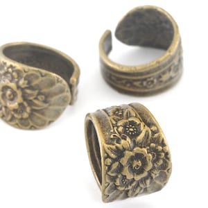 May include: Three antique gold-toned metal rings with floral designs. The rings are open and can be used as decorative embellishments for jewelry or crafts.