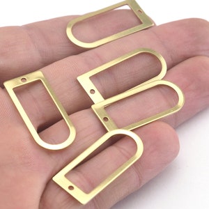 May include: Five gold-colored metal rectangular frames with rounded corners and two holes on each side. The frames are arranged in a pile on a hand.