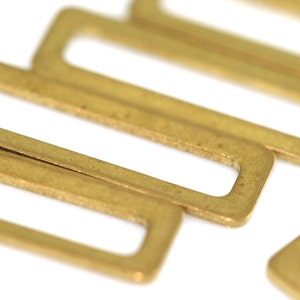 Pode incluir: Um close-up de várias fivelas deslizantes retangulares de metal dourado. As fivelas estão dispostas em um padrão escalonado.