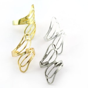 May include: Two pairs of open-design rings in gold and silver. The rings feature a series of curved, wing-like shapes, creating an airy and elegant aesthetic. The rings are displayed on a white background.